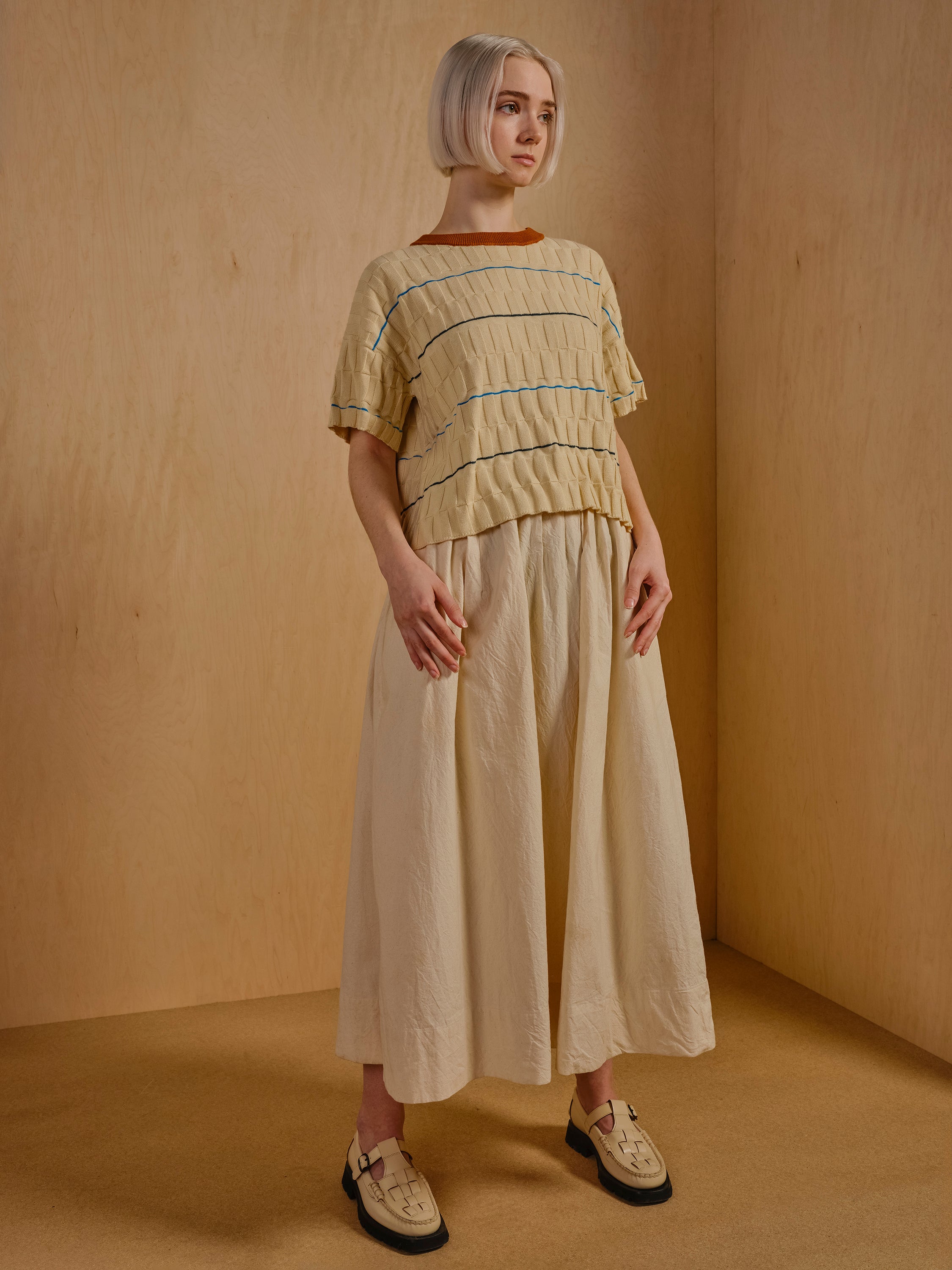 The Wiggle Stripe Knit Grid Tee modeled with a white skirt is part of The Endery's sustainable knitwear collection.