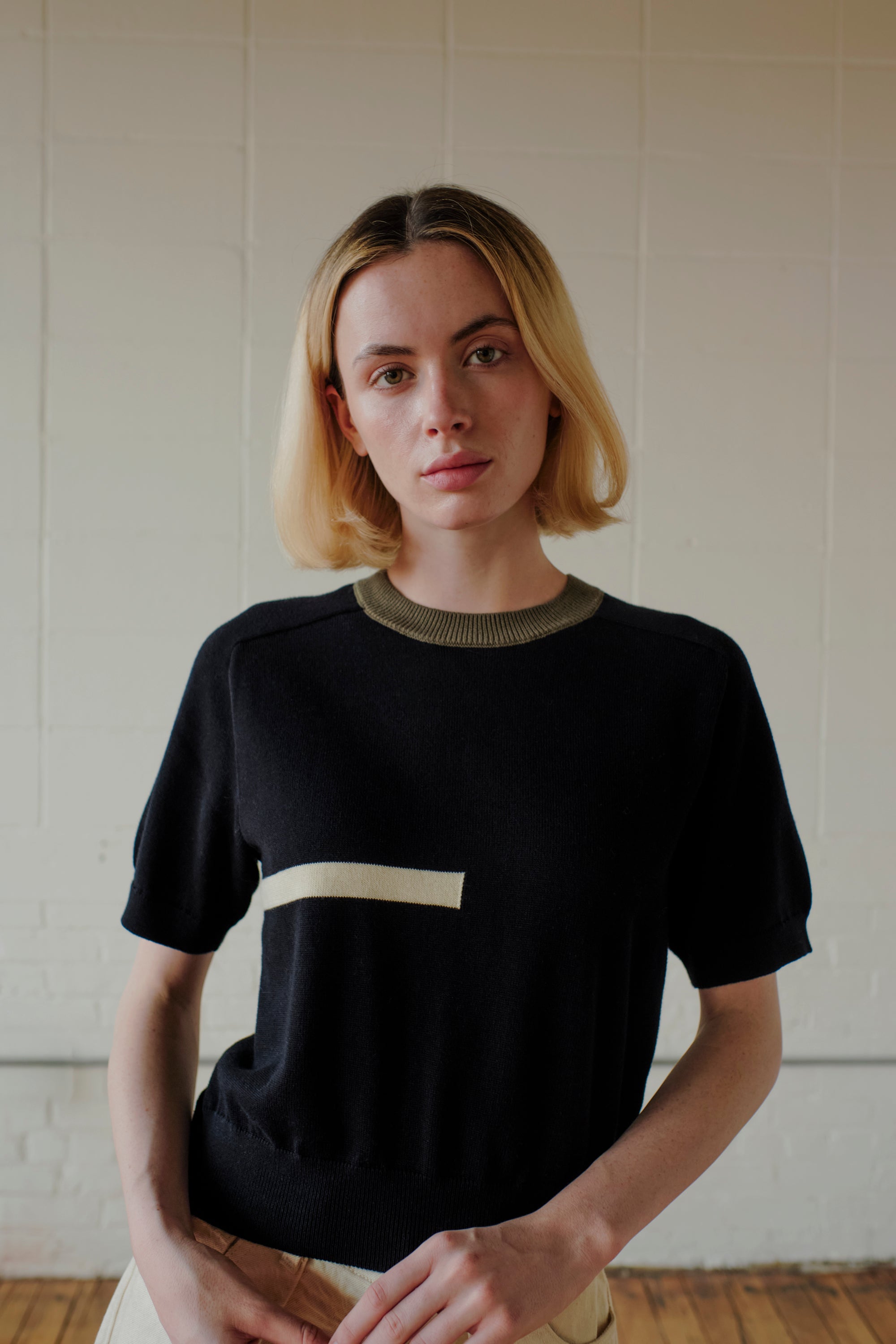 Woman wearing a black t-shirt with a white square design against a plain wall.